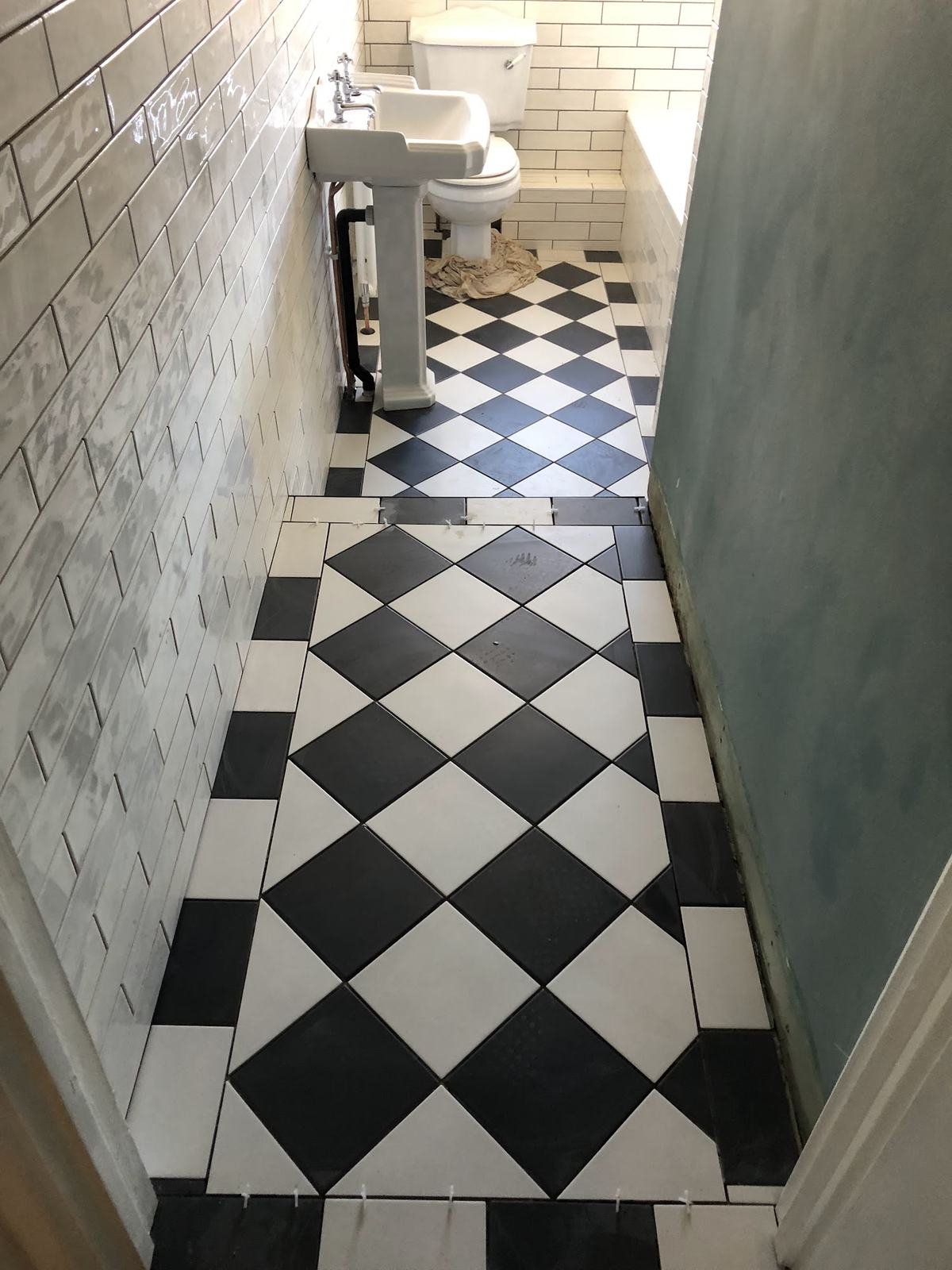Small bathroom with a black and white chequer floor and white metro walls