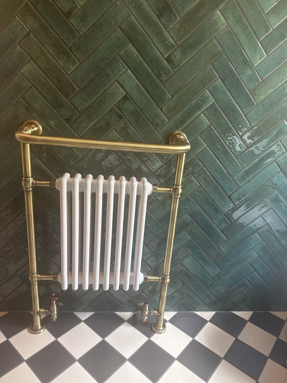 Green gloss tiles in herringbone behind a brass towel radiator