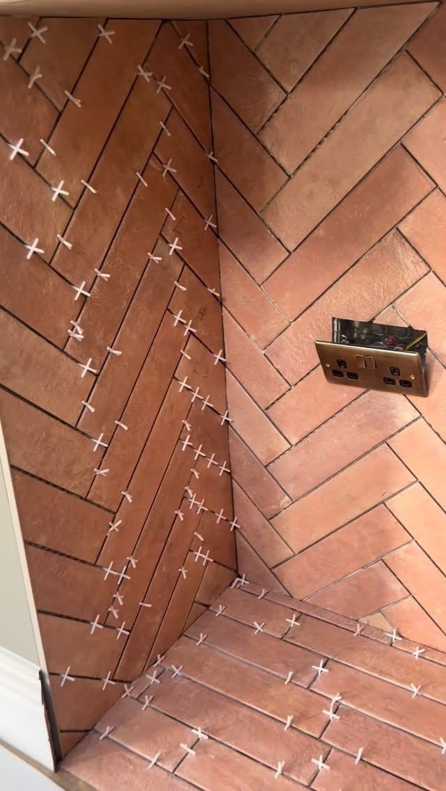 Terracotta-coloured herringbone tiles going up round a fireplace, with spacers still in