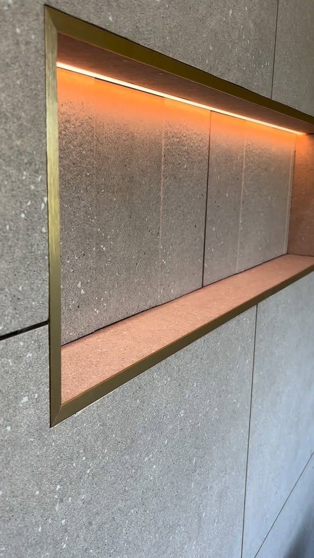 Recessed shower niche lit with a warm LED strip and metal trim