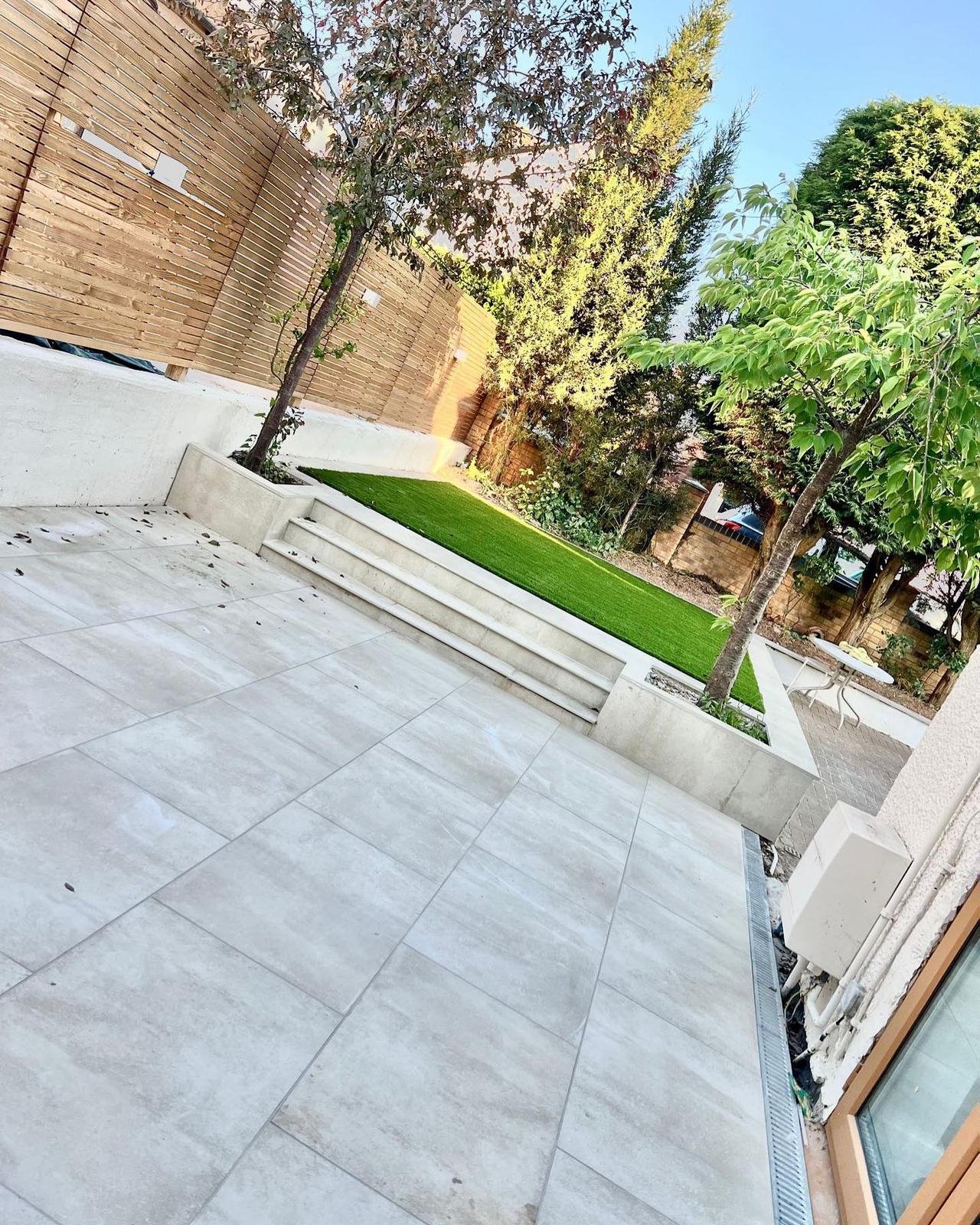 Pale porcelain patio with steps up to an artificial lawn