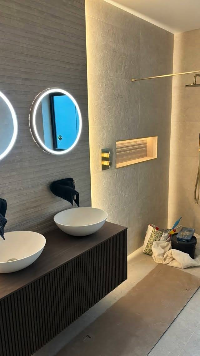 Wet room with twin basins, round lit mirrors and a lit niche